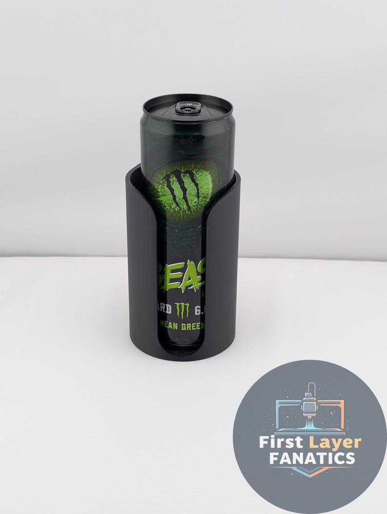 May include: A black can cooler holding a green and black Monster Energy drink can. The can cooler has a curved design with a cutout to reveal the can's label. The drink can features the Monster Energy logo.