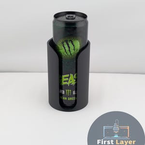 May include: A black can cooler holding a green and black Monster Energy drink can. The can cooler has a curved design with a cutout to reveal the can's label. The drink can features the Monster Energy logo.