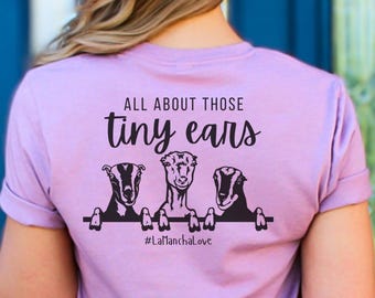 Peut inclure: T-shirt lilas avec l'inscription "ALL ABOUT THOSE tiny ears" et trois illustrations de chèvres. Le t-shirt porte également le hashtag "#LaManchaLove" imprimé sous les chèvres.