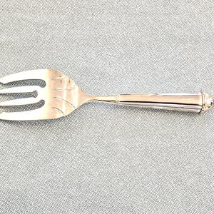 Op de afbeelding: Een zilveren serveervork met drie tanden en een decoratief handvat. De vork is gemaakt van glanzend metaal en ligt op een grijze ondergrond. De tanden hebben een bladachtig ontwerp.