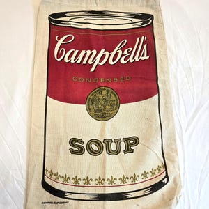 Könnte beinhalten: Beige Tragetasche mit einem Campbell's Soup-Dosen-Design. Das Design umfasst das Campbell's-Logo in Weiß, einen roten Hintergrund und das Wort "SOUP" in Gold. Die Tasche hat einen Kordelzugverschluss.
