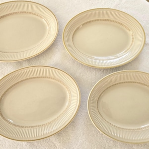 以下が含まれることがあります： クリーム色の楕円形のサービングプラッター4枚。金色の縁取りがあり、縁の近くに装飾的な金色の模様があります。各プラッターは、縁にリブ模様のデザインが施されています。白い表面に配置されています。