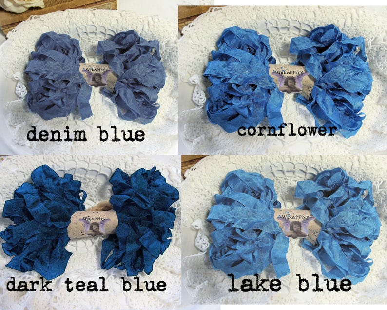May include: Four bundles of blue fabric ribbon in denim blue, cornflower, dark teal blue, and lake blue. Each bundle is arranged on a white lace surface and labeled with its color name. The ribbons are ruffled and textured.