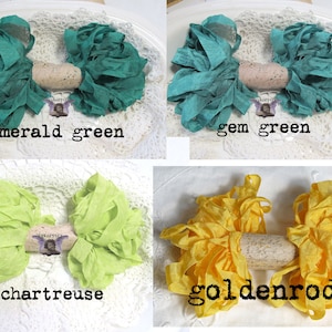 May include: Four handmade ribbon bows in emerald green, gem green, chartreuse, and goldenrod. Each bow is centered with a cork and displayed on a white lace surface. Text on the image reads "emerald green", "gem green", "chartreuse", and "goldenrod".