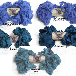 May include: Five bundles of ruffled fabric ribbon in shades of blue and teal. The colors are sapphire, glory, teal, blueberry, and tranquil sea. Each bundle has a decorative tag with the text "Wicked Pixy".
