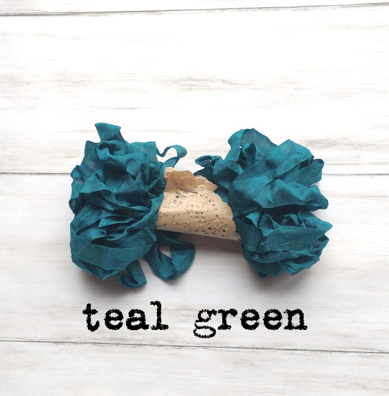 May include: Teal green fabric ribbon with a ruffled texture, paired with a beige lace element. The text "teal green" is printed in black below the ribbons. The ribbons are arranged on a white wooden surface.