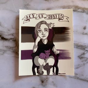 May include: Illustration of a person seated in a chair, with three cats. The person is wearing a black top and has a tattoo on their arm. The text "ACE OF SPAYEDS" is above the person. The background has a color gradient of black, gray, and purple.