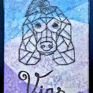 Può includere: Opera d'arte incorniciata raffigurante il volto di un cane creato con filo nero su un disegno geometrico. Lo sfondo ha un gradiente blu e viola con accenti glitterati. Il nome "Vias" è scritto in corsivo.