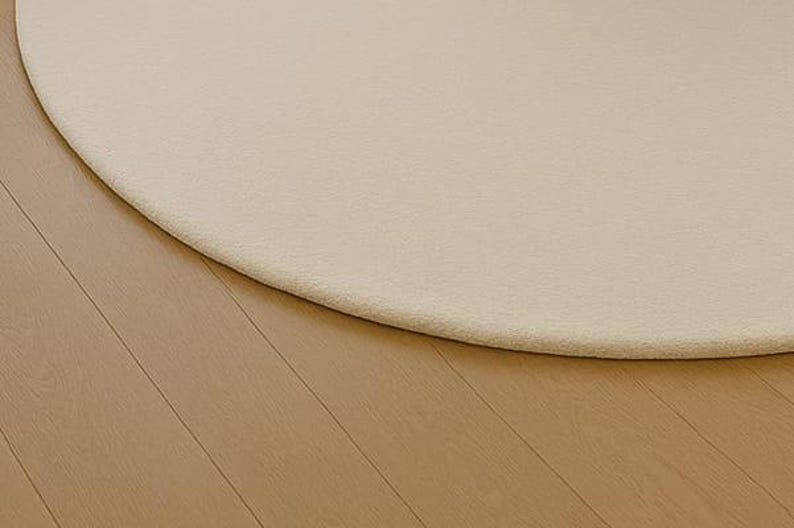A modern white round rug placed in a beige living room beside large windows with pool and garden view. The soft wool-blend carpet sits under a marble coffee table and cream sofa, creating a bright, elegant, and minimalist interior. Perfect for contemporary, Scandinavian, or neutral-style homes.