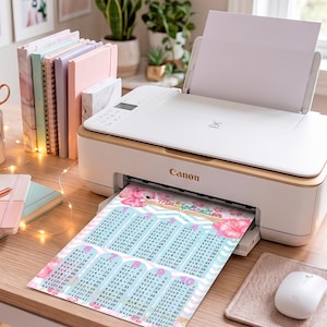 Puede incluir: Una impresora Canon blanca sobre un escritorio imprime una hoja con una tabla de multiplicar. El gráfico muestra los números del 1 al 10 con detalles florales rosas y un patrón de chevrón, exhibiendo ecuaciones matemáticas sobre un fondo azul claro.