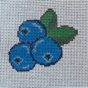 May include: Cross-stitch design featuring three blue blueberries with dark centers and a green leaf. The blueberries are stitched with varying shades of blue thread, and the leaf is stitched with green thread. The design is on a white background.
