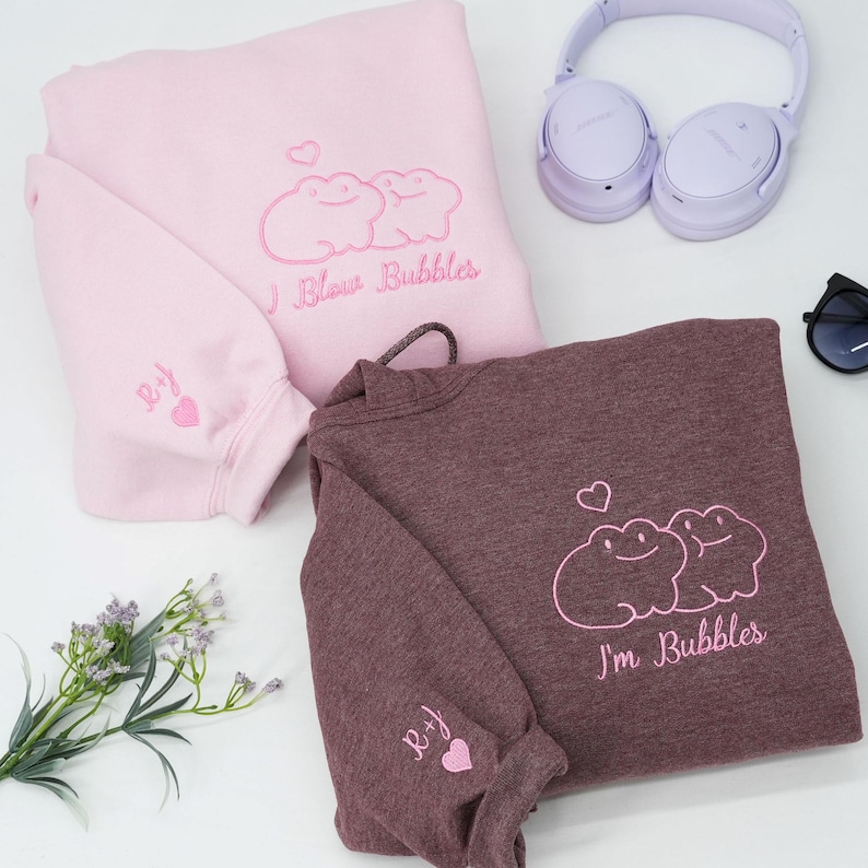 May include: Two sweatshirts, one pink and one maroon, with embroidered frog designs and text. The pink sweatshirt says "I Blow Bubbles," and the maroon one says "I'm Bubbles." Both have matching embroidered initials and hearts on the sleeves.