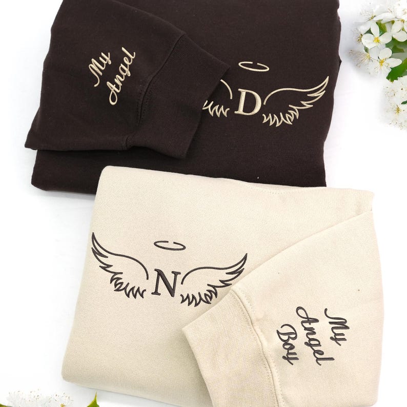 dark chocolate and sand sweatshirts embroidered in cream and dark brown threads. The “D” and “N” initials are paired with phrases like “My Angel” and “My Angel Boy” on the sleeves, creating a heartfelt, cozy tribute design.
