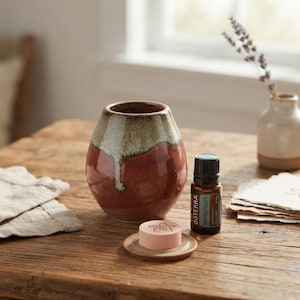 May include: A ceramic vessel with a two-tone glaze of reddish-brown and cream, a small round ceramic disc featuring a flower engraving, and a brown glass essential oil bottle labeled dōTERRA spearmint with a black screw-top cap.