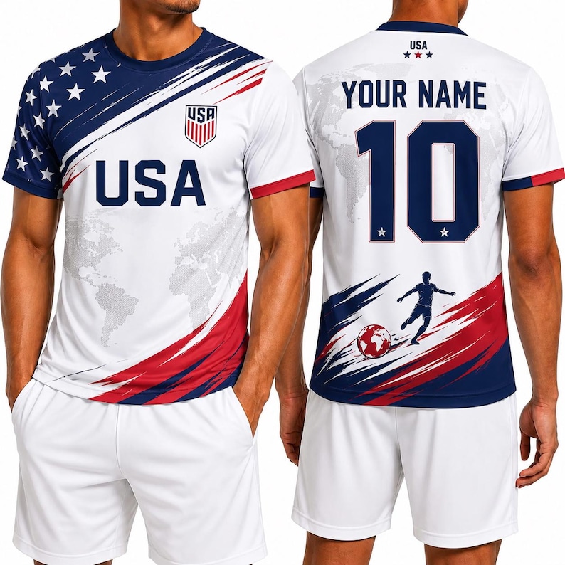 May include: White soccer jersey with blue and red accents, featuring the word "USA" and a shield logo. The jersey has a map design and stars on the sleeves. The back displays "YOUR NAME" above the number "10" and a soccer player graphic.