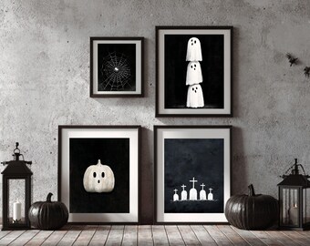 May include: Halloween-themed wall art featuring framed prints of a spiderweb, stacked ghosts, a pumpkin, and a graveyard scene. Decorative black pumpkins and lanterns with candles complete the spooky decor.