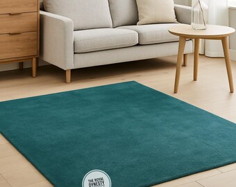 Puede incluir: Alfombra rectangular de color turquesa. Está colocada sobre un suelo de madera clara en un salón. La alfombra tiene una textura suave y afelpada. El logotipo de The Royal Dynasty Carpet es visible.