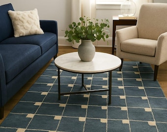 Könnte beinhalten: Ein Wohnzimmer mit einem marineblauen Sofa, einem cremefarbenen Kissen und einem beigefarbenen Sessel. Ein runder Couchtisch mit Marmorplatte steht auf einem blauen Teppich mit geometrischem Muster. Der Boden ist aus Holz.