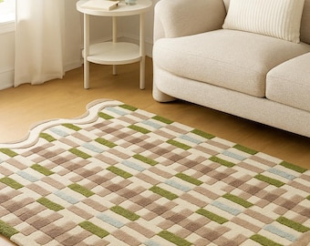 May include: A rectangular area rug with a geometric pattern in shades of beige, brown, green, and light blue. The rug has a scalloped edge and is placed on a hardwood floor, near a beige sofa.