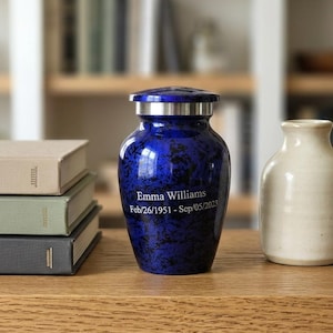 Könnte beinhalten: Eine Urne mit blau-schwarzem Marmormuster und einem silberfarbenen Metalldeckel. Auf der Vorderseite ist der Text Emma Williams sowie die Daten Feb/26/1951 - Sep/05/2023 in einer klaren, weißen, serifenlosen Schriftart eingraviert.