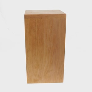 May include: A rectangular wooden box with a light brown finish. The box has a simple, minimalist design with clean lines and a smooth surface. The wood grain is visible, adding texture to the piece. The box is likely used for storage or display.