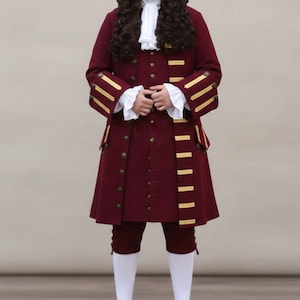 Puede incluir: Un disfraz colonial burdeos con un abrigo largo con ribetes dorados, calzones a juego y una camisa blanca con volantes. El atuendo incluye una peluca marrón oscuro, medias blancas y zapatos negros. Este disfraz histórico es adecuado para cosplay o producciones teatrales.