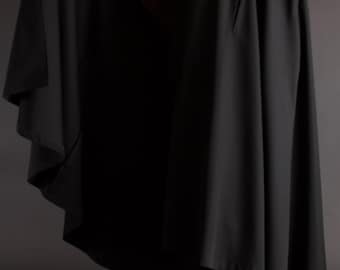 May include: A long, black hooded cloak. The cloak is made of a smooth, dark fabric and drapes to the ankles. The cloak is worn over a white collared shirt and black suit. The image is set against a dark gray background.