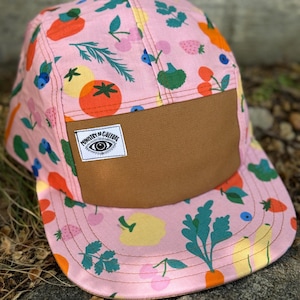 May include: A pink and brown 5-panel hat with a fruit and vegetable print. The hat has a brown brim and a patch that says "Ministry of Culture".