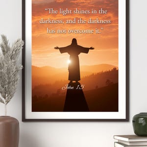 Peut inclure: Impression encadrée montrant une silhouette avec les bras tendus sur un fond de coucher de soleil. Le texte "La lumière luit dans les ténèbres, et les ténèbres ne l'ont point vaincue." et "Jean 1:5" sont affichés.