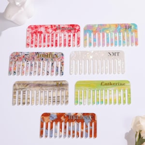 May include: A collection of colorful hair combs with personalized text. The combs feature various patterns, including red, white, and blue, and a mix of pastel colors. Each comb has a unique name or initials engraved on it.