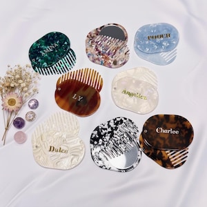 May include: A selection of personalised compact mirrors and combs in diverse colours and patterns. Each compact features a comb and mirror, with names such as "Amina" and "Charlee" in gold lettering. Designs include green, tortoiseshell, and marbled patterns.