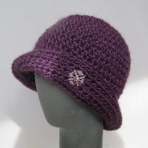 May include: A purple crocheted cloche hat with a decorative flower brooch.
