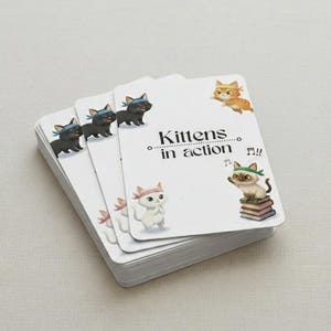 Puede incluir: Una pila de cartas blancas con esquinas redondeadas. Cada carta presenta gatitos de dibujos animados en varias poses, con cintas para la cabeza. El texto "Kittens in action" está impreso en una carta. También hay notas musicales.