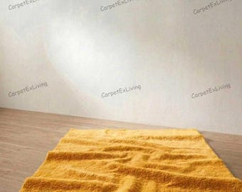 May include: A mustard yellow rectangular rug with a textured surface is on a wooden floor. Above the rug, a bronze-colored curtain rod is mounted on a white wall. The rod has decorative finials on each end.