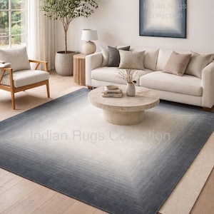 Pode incluir: Sala de estar com um tapete retangular grande com um design gradiente, passando de uma borda azul escura para um centro creme claro. O quarto inclui um sofá branco, uma mesa de centro redonda e uma obra de arte emoldurada.