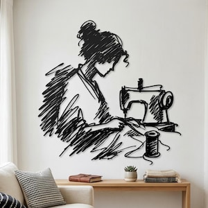 May include: A black metal wall art piece featuring a stylised, scribbled-line illustration of a person with hair in a bun operating a sewing machine, with a spool of thread positioned in the foreground, creating a continuous sketch-like aesthetic.