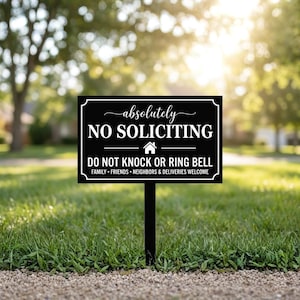 May include: A black and white sign in a yard with the words "absolutely NO SOLICITING" and "DO NOT KNOCK OR RING BELL". The sign also states "FAMILY • FRIENDS • NEIGHBORS & DELIVERIES WELCOME". The sign is mounted on a black stake.