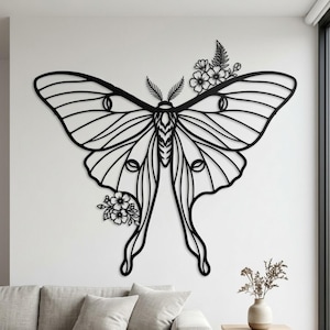 May include: Black metal wall art of a large moth with intricate wing details and floral accents. The moth's wings are spread wide, and the design includes delicate lines and curves. The artwork is mounted on a white wall.