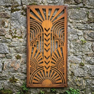 Könnte beinhalten: Ein rechteckiges, rostfarbenes Metall-Wandkunstwerk mit einem Sonnenstrahl-Design. Die Kunst zeigt ein symmetrisches Muster aus radialen Linien, Bögen und geometrischen Formen, montiert an einer verwitterten Steinmauer. Das Stück ist mit sichtbaren Nieten befestigt.
