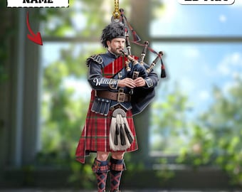 May include: A 2D flat ornament depicting a bagpiper in traditional Scottish dress. The ornament shows a man in a red and blue tartan kilt, playing the bagpipes. The ornament has the text "CUSTOM NAME" and "2D Flat".
