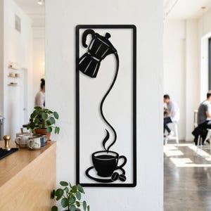 Könnte beinhalten: Ein schwarzes Wandkunstobjekt aus Metall mit einem rechteckigen Rahmen, der die Silhouette einer Mokkakanne zeigt, die Flüssigkeit in eine Tasse auf einer Untertasse mit zwei Kaffeebohnen gießt, verbunden durch einen durchgehenden Strahl.