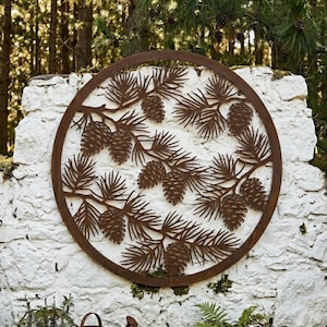May include: A circular, rust-coloured metal wall art piece featuring a detailed cutout design of pine branches and pinecones. The artwork is mounted on a white stone wall, creating a contrast of textures and colours. The design evokes a natural, rustic aesthetic.