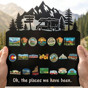 Puede incluir: Tablero de exhibición de metal negro con una silueta de montaña y autocaravana, que contiene coloridos pines de esmalte de parques nacionales y destinos de viaje. El texto "Oh, the places we have been.." está en la parte inferior.