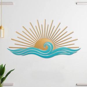 May include: A wall-mounted metal art piece depicting a sunrise over ocean waves. The sun is a golden color with radiating beams. The waves are a teal blue color, adding a coastal theme to the decor.