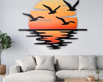Puede incluir: Arte mural de metal que representa una escena de atardecer. La obra presenta un sol naranja y amarillo, siluetas negras de pájaros en vuelo y el reflejo del atardecer en el agua. Montado en una pared de ladrillo blanco.