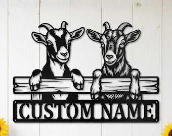 May include: Black metal wall art featuring two goats peering over a wooden fence. The goats have detailed features and are positioned above a rectangular sign that reads "CUSTOM NAME". The artwork is designed for personalization.