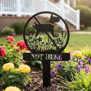 May include: Black metal garden stake featuring a dog silhouette within a crossed-out circle, with the words "NOT HERE" cut out. The sign is set in a garden with vibrant flowers. The stake is designed to deter dogs.