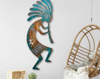Puede incluir: Arte de pared de metal que representa una figura de Kokopelli, un símbolo nativo americano. La obra de arte presenta una combinación de colores turquesa y cobre con patrones geométricos. La figura toca una flauta, con un tocado decorativo.