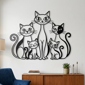 Puede incluir: Una pieza de arte mural de metal negro que representa una familia de cinco gatos estilizados. Los gatos están representados en un estilo minimalista con diferentes poses y expresiones. La obra de arte está montada en una pared blanca.