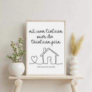 May include: A framed print with the text "nil aon tinteán mar do thinteán féin" and "THERE IS NO PLACE LIKE HOME". The artwork features a line drawing of a house and heart. The frame is light-coloured, and the background is white.